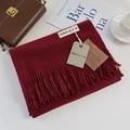 Detail view of wine red cashmere-feel scarf with tassels and branding tags on desk - Burgundy / 200cm