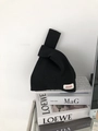 Detail of black waffle knit handbag with red label on a minimalist indoor desk - Black