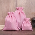 Three pink linen drawstring jewelry bags in different sizes on a rustic wooden surface - Pink