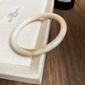 Close-up of vintage resin bangle with beige marble texture on a textured display stand - Off White