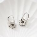 Boucles d'oreilles créoles fleurs en acier inoxydable argenté sur fond céramique blanc - Couleur Acier