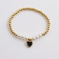 Elegant gold beaded bracelet with white pearls and a black heart charm on grey surface - Black