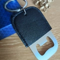 Detail of a stainless steel bottle opener with black PU leather keychain on a wood desk - Large / Black