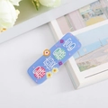 Detail of light blue matte hair clip with stylized red and green text characters - Slim and Rich