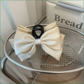 Close-up of a large cream satin bow hair claw clip placed in a silver metal basket - Off White