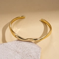 Vista dettagliata del bracciale aperto ondulato placcato oro 18k su espositore in pietra - Oro