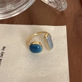 Detail shot of golden open ring with blue round stone and grey rectangular gem on textured paper - Adjustable Open / Blue Grey Enamel Style