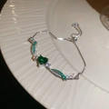 Detalle macro de pulsera plateada con corazón de circón verde y piedras brillantes - Plata-Verde