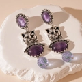 Gros plan sur des boucles d'oreilles argentées vintage avec motif chat et résine mauve - Style Ovale Chat Argenté Violet