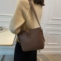 Chic brown leather bucket bag with decorative buckle worn by model on shoulder - Coffee