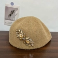 Detail of khaki wool beret showing shiny gold sequins and ornate feather rhinestone brooch - Camel