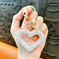 Portachiavi a cuore dorato con strass di cristallo e chiusura a moschettone tenuto in mano - Bianco