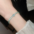 Close-up of 18K gold plated bracelet with emerald green zircon crystals on a wrist - Blue