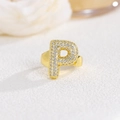 Macro di anello dorato con lettera P e zirconi incastonati su sfondo bianco puro - Lettera P