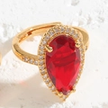 Nahaufnahme eines Goldrings mit birnenförmigem rotem Edelstein und Zirkonia-Halo - Birnenförmiger Stil / Roter Wassertropfen