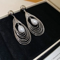 Detailed view of silver layered hollow teardrop pearl earrings on black velvet - Silver