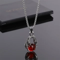 Détail d'un pendentif griffe de dragon argentée tenant une sphère en pierre rouge - Griffe de Bête Perle Rouge