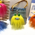 Macro shot of fluffy yellow monster keychain with green pom-poms on blue denim bag - Single Piece / Yellow