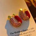 Macro shot of U-shaped gold earrings with pink gemstones and red enamel on an art card - U-Shape Gem Ear Buckle / Rose Red