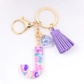 Macro detail of resin letter J keychain with purple tassels and star sequins - Letter J