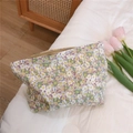 Détail d'une trousse à maquillage en coton à fleurs mauves sur un fond de lit blanc - Base Violet Clair avec Motif Floral Vert