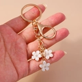 Detail of white enamel cherry blossom flowers on a gold metal keychain accessory - White