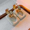 Close-up of golden C-shaped hoop earrings with cream rectangular resin pendants on a tray - Beige (Silver Earring Post)