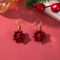 Detail shot of festive red bow earrings with gold hooks on a pine branch background - D1301 (Red Flower Ball)