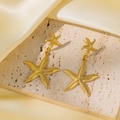 Détail de boucles d'oreilles étoile de mer dorées 18k sur pierre et soie beige - Boucles d'Oreilles Pendantes Double Étoile de Mer (QYG89) / Or