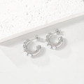 Silver C-shaped stainless steel earrings with white pearls on a textured stone background - Steel