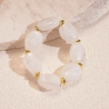Detalle de pulsera acrílica ovalada irregular con acentos dorados sobre base de piedra - Blanco