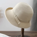 Hepburn style beige straw sun hat with rolled edge on a wooden stand in a soft studio setting - Beige
