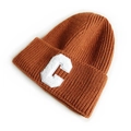 Caramel knitted beanie hat with white fuzzy letter C patch on clean background - Coffee