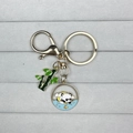 Golden panda keychain with green bamboo and blue enamel round charm on velvet base - Panda Catching Fish