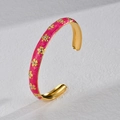 Gouden open armband met roze emaille bloemen en kristallen op witte textuur - Rozerood