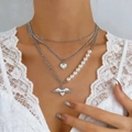 Three-layer silver necklace with faux pearls and heart wing pendant worn by a model - Triple Silver Pearl Wing Heart Pendant Style