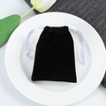 Detail of a black velvet drawstring pouch with white satin ribbon on a white ceramic tray - Black