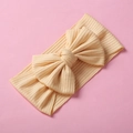 Beige ribbed knit baby headband featuring a large bow on a soft pink background - Beige