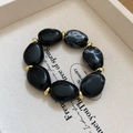 Macro view of irregular acrylic beaded bracelet with black pebbles and golden spacers - Black