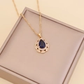 Close-up of a gold teardrop necklace with blue crystal and small pavé stones in a gift box - Royal Blue