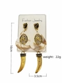 Detailweergave van retro oorbellen met hoefijzermotief en slagtand hanger. - Gouden Slagtand Wit Paardenkop