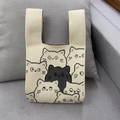 Off-white knitted wrist bag featuring pixel-style cat patterns on a gray fabric sofa - Beige Cat Pattern