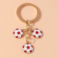 Detailed close-up of golden metal keychain featuring three red and white football pendants - Red