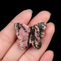 Pink agate crystal butterfly carving with black veins held in hand on dark background - Rhodonite / 30*35mm No Hole