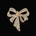 Dettaglio di una spilla a fiocco dorata con strass scintillanti su sfondo nero lucido - Stile B220