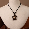 Maori style resin sea turtle pendant on black woven cord displayed on a linen mannequin - Turtle