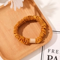 Detail of a ginger yellow satin scrunchie with a stylish rectangular resin buckle ornament - Tencel Velvet Ginger