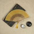 Yellow silk folding fan with bamboo frame and matching tassel on a textured background - Yellow / 23CM