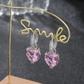 Dettaglio di orecchini a cuore rosa con zirconi appesi a un elegante supporto dorato - Rosa argento