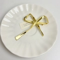 Dettaglio macro di una spilla a fiocco in metallo dorato di qualità su piatto in ceramica - Oro